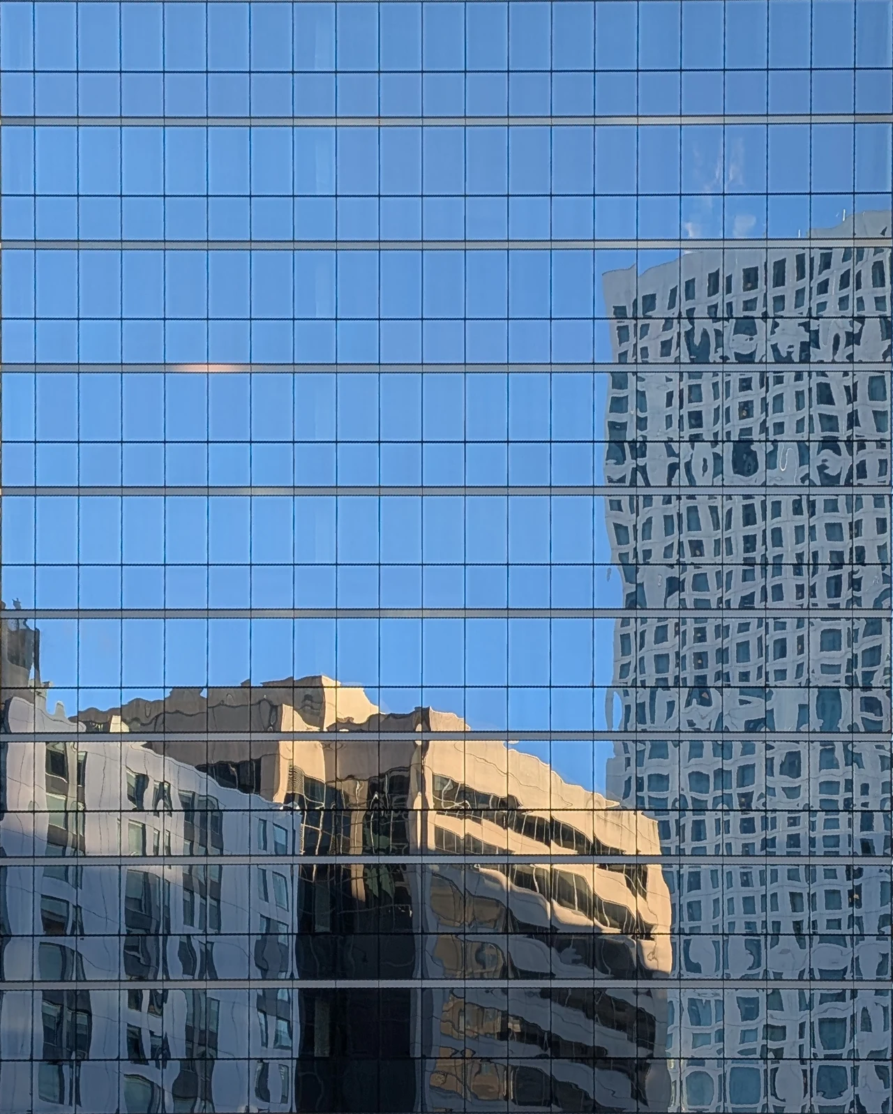 A blue glass facade collecting fragments of nearby architecture.